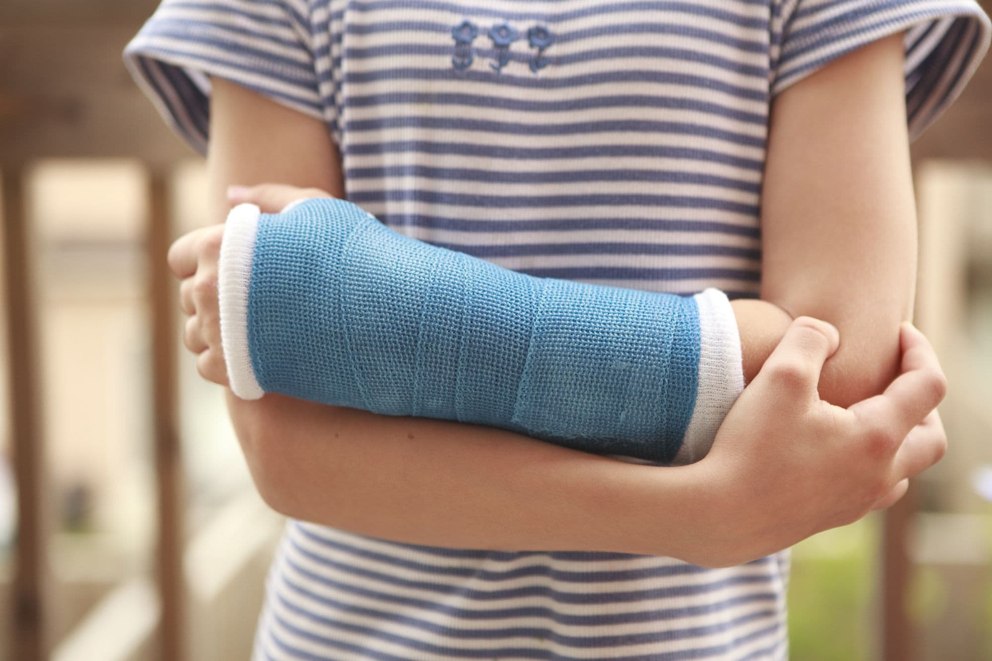 A child's forearm in a blue cast, supported by both hands