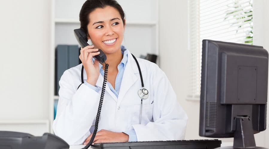 A clinician in a white coat taking a call at the front desk